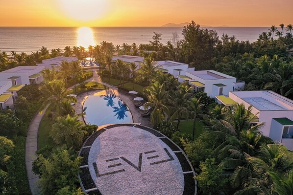 Un resort con piscina central, rodeado de palmeras y edificios modernos.