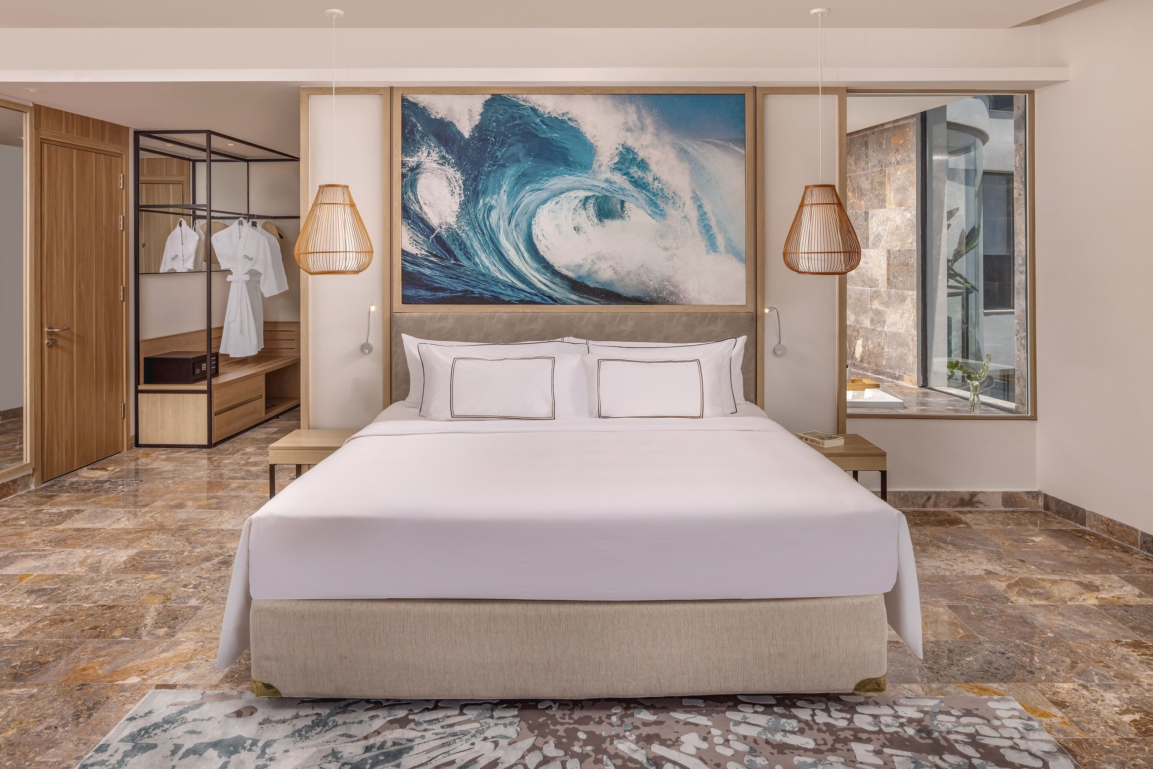 A modern bedroom with a large bed, a wardrobe, a mirror, and a painting of a wave.