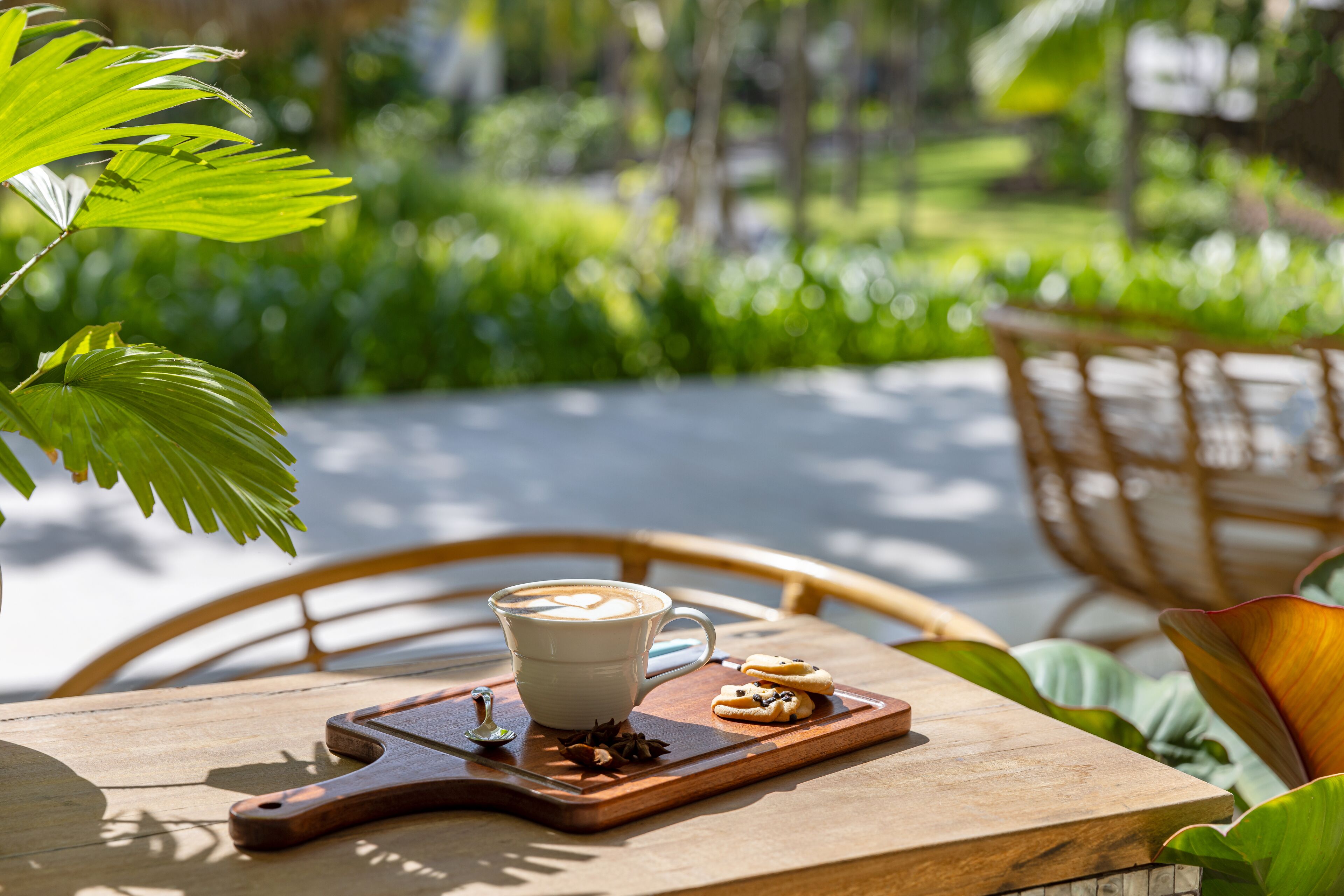 A wooden table with a white cup of coffee, a wooden spoon, and two cookies on a wooden board.