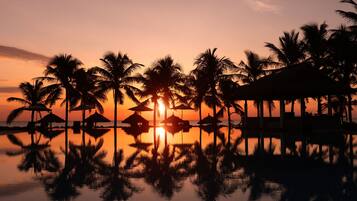 Un atardecer sobre una masa de agua tranquila, con palmeras y bungalows sobre el agua.
