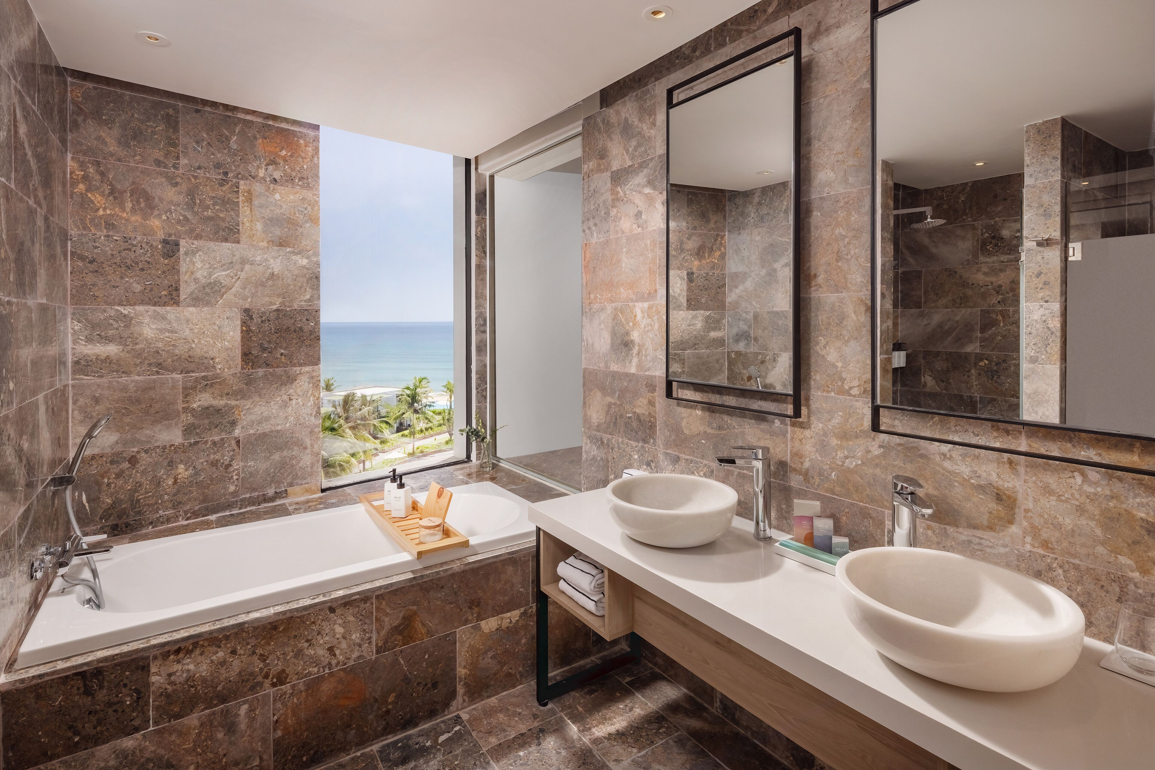 Un baño moderno con una bañera grande, dos lavamanos y vista al océano.