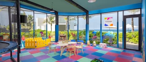 Zona de juegos infantiles con mesa de billar, alfombras de colores y vistas al océano.