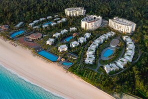Vista aérea de un complejo turístico con varias edificaciones, piscinas y una playa.