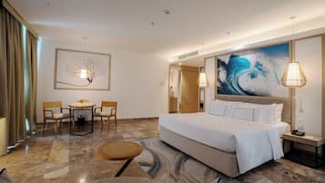 A hotel room with a large bed, a dining table with chairs, a small round table, and a large abstract painting on the wall.