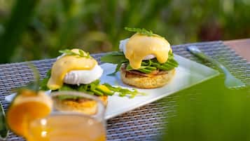 A breakfast setting with eggs benedict on a white plate, garnished with greens, and a glass of orange juice.
