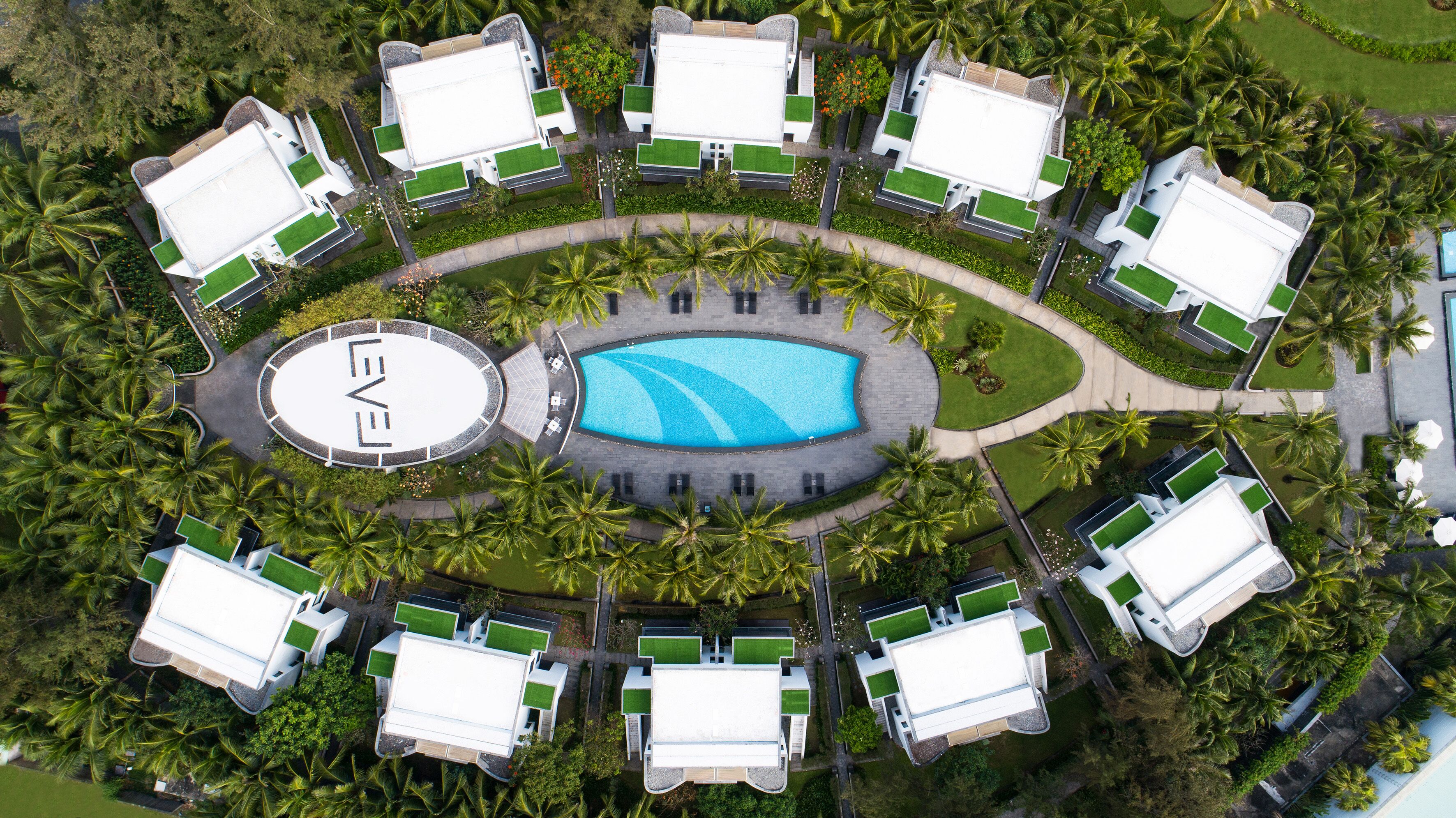 Vista aérea de un complejo turístico con una piscina central, rodeado de varias villas con piscinas privadas y abundante vegetación.