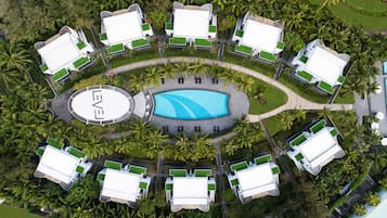Vista aérea de un complejo turístico con una piscina central, rodeado de varias villas con piscinas privadas y abundante vegetación.