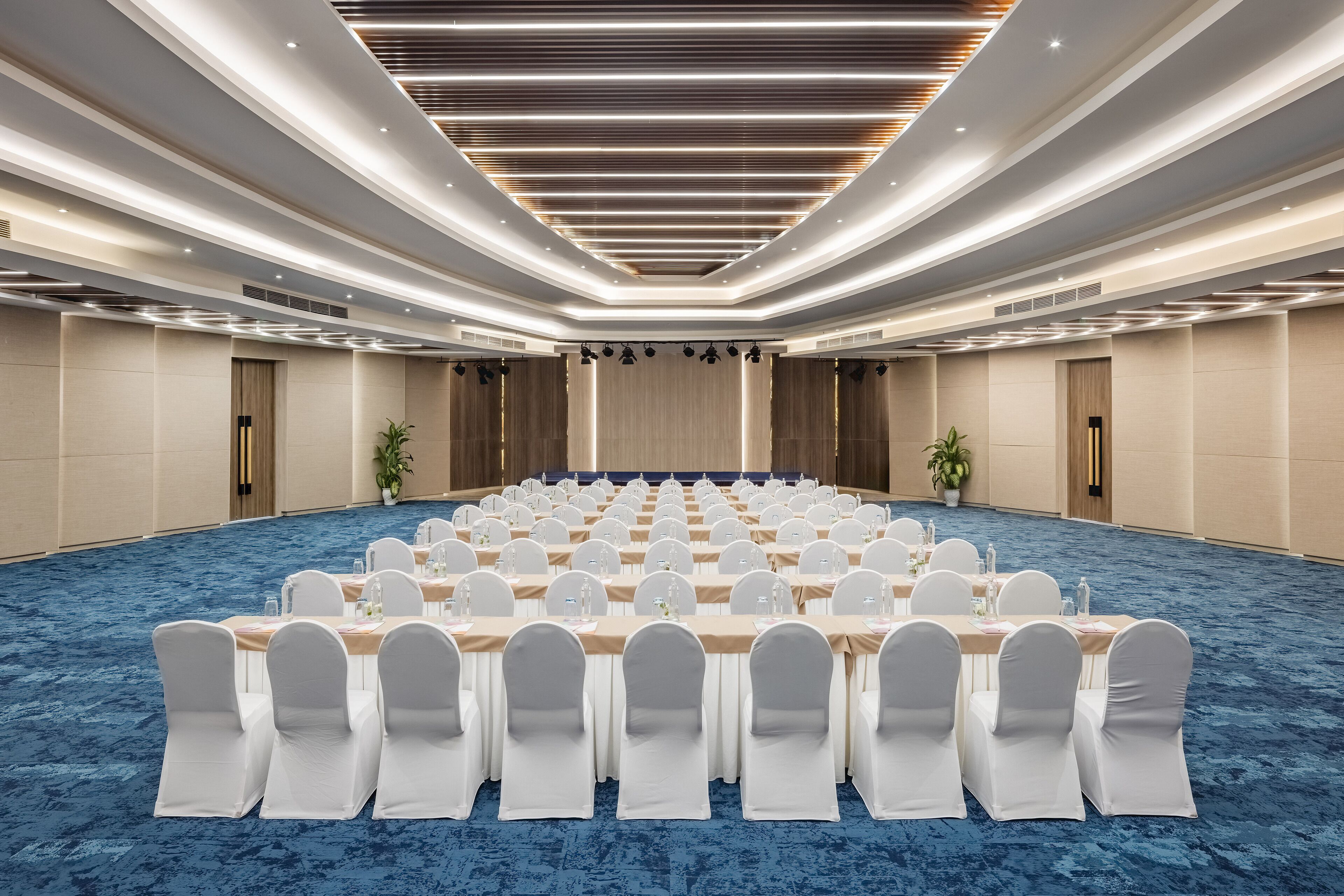 A conference room with rows of tables and chairs, a blue carpet, and a modern ceiling design.