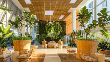 A spacious indoor area with wooden furniture, large potted plants, and a ceiling with geometric patterns.