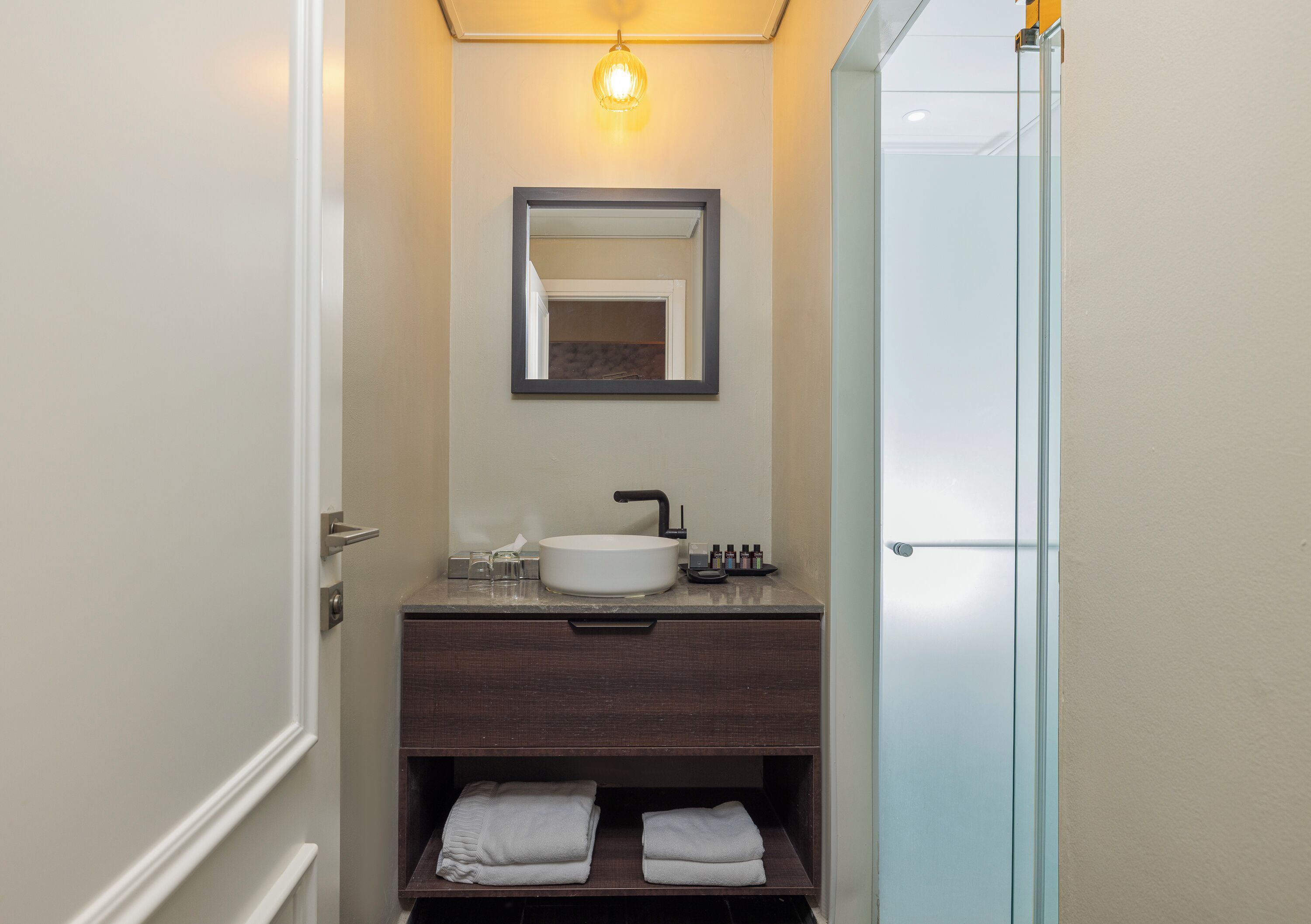 Un baño con lavamanos blanco, tocador oscuro, un espejo y puerta de ducha de cristal.
