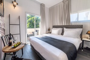 Quarto de hotel com uma cama grande, uma mesa pequena com uma garrafa e copos, e vista para o verde lá fora.