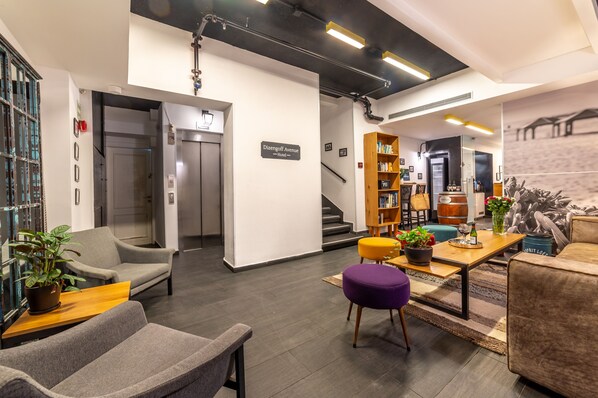A modern hotel lobby with a reception desk, seating area, staircase, and a bookshelf. - Dizengoff Avenue Boutique Hotel - by Echo Hotels (Tel Aviv)