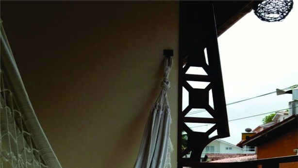 A hammock hanging on a wall in a room with tiled flooring and a wooden structure in the background. - Pousada Estevao (Cairu)