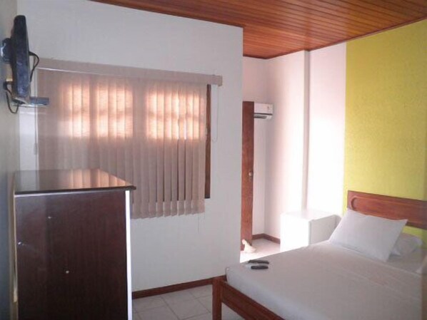 A hotel room with a wooden ceiling, a bed with white bedding, a desk with a computer, and a window with vertical blinds. - Pousada Estevao (Cairu)