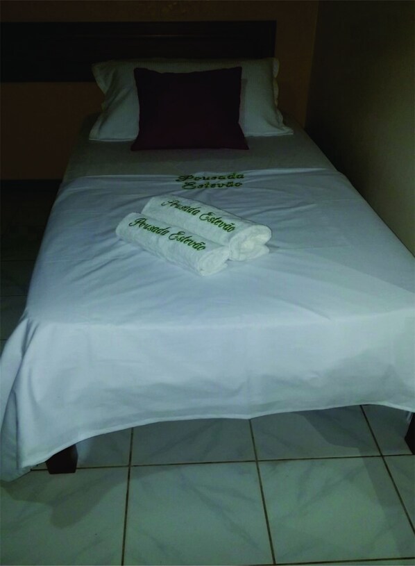 A single bed with a white bedspread and two folded towels with embroidered text.