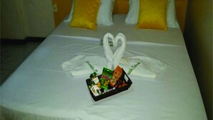A neatly made bed with white linens, two yellow pillows, and a heart-shaped towel arrangement on the bedspread. - Pousada Estevao (Cairu)