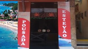 A hotel entrance with a sign reading "Pousada Estevão" and a view of a beach with palm trees and boats. - Pousada Estevao (Cairu)