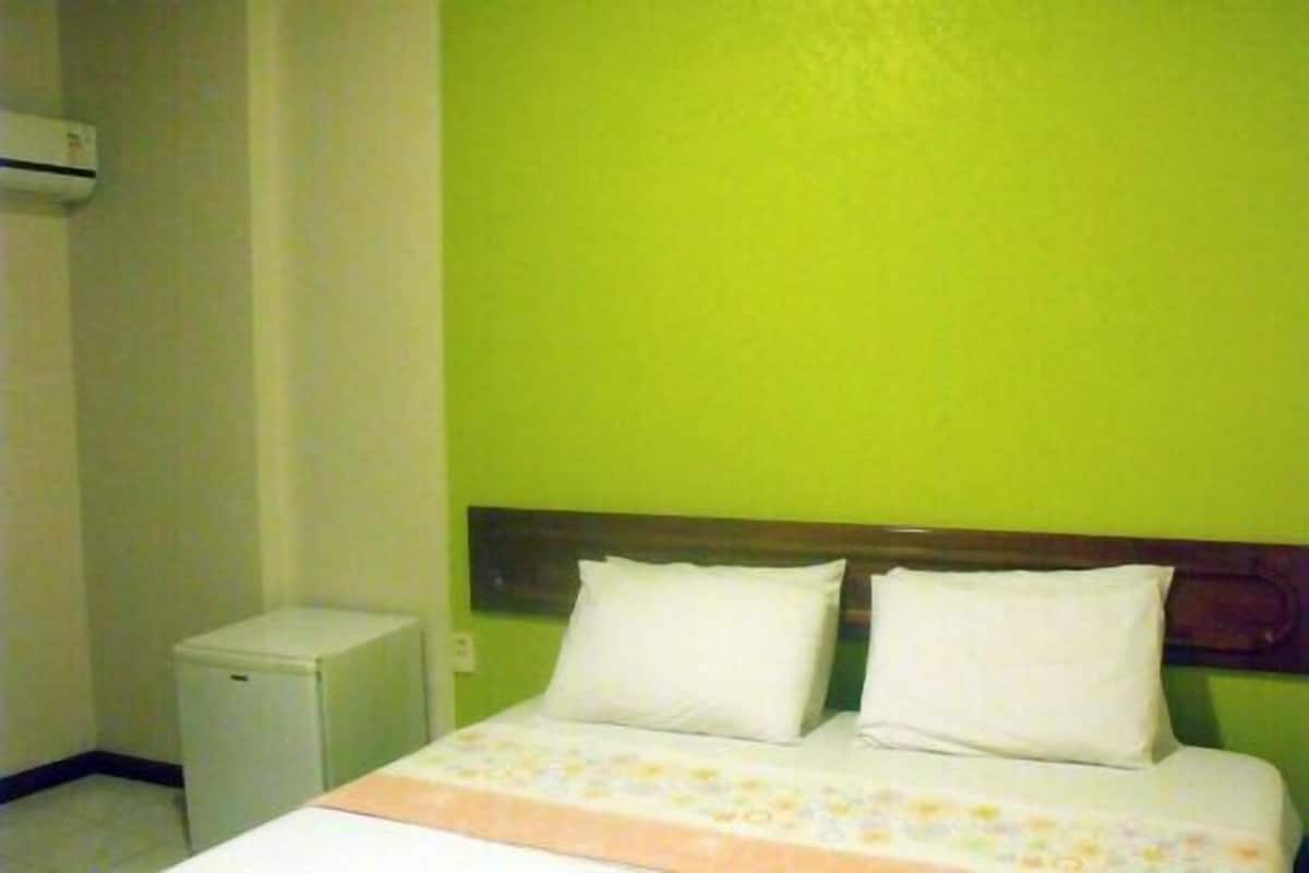 A room with a bed, a small white cabinet, and a green wall.
