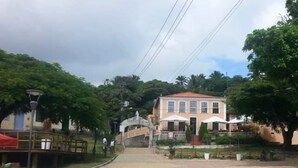 A paved walkway leading to a building with a tiled roof, surrounded by greenery and a clear sky. - Pousada Estevao (Cairu)
