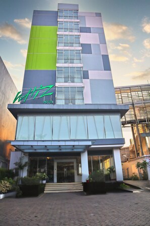 Un hotel moderno con una fachada destacada en verde y gris, amplias ventanas y una entrada bien iluminada.