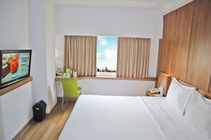 Habitación de hotel con cama, escritorio, silla, televisión y ventana con cortinas.