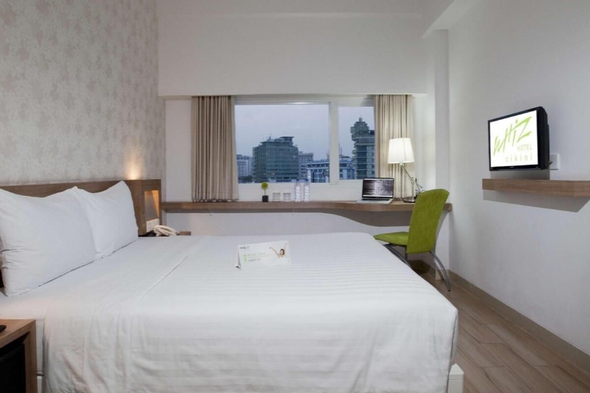 Una habitación de hotel con una cama grande, un escritorio con computadora, un televisor y una ventana con vista a la ciudad.