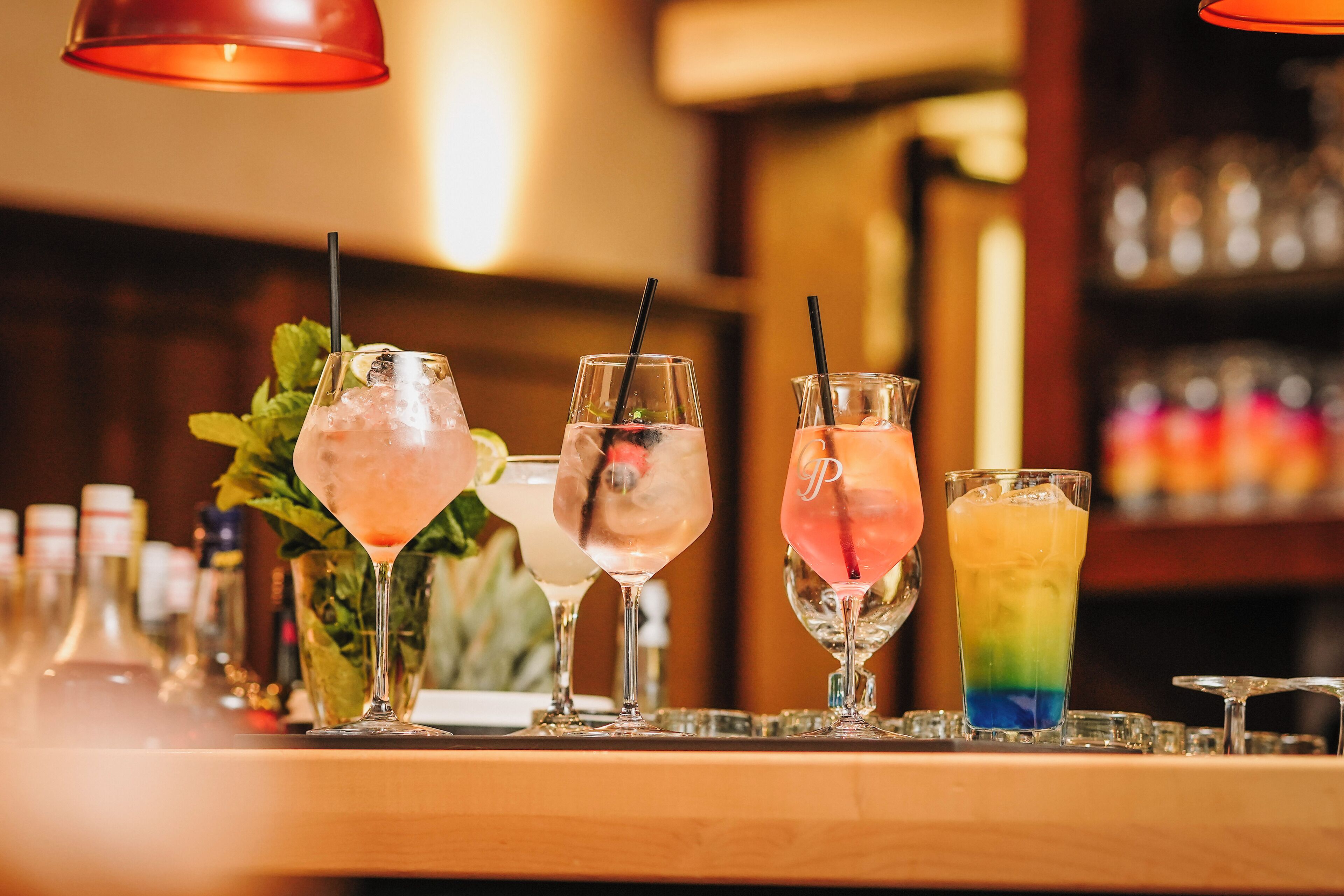 Un comptoir de bar avec divers cocktails et, en arrière-plan, une sélection de bouteilles.