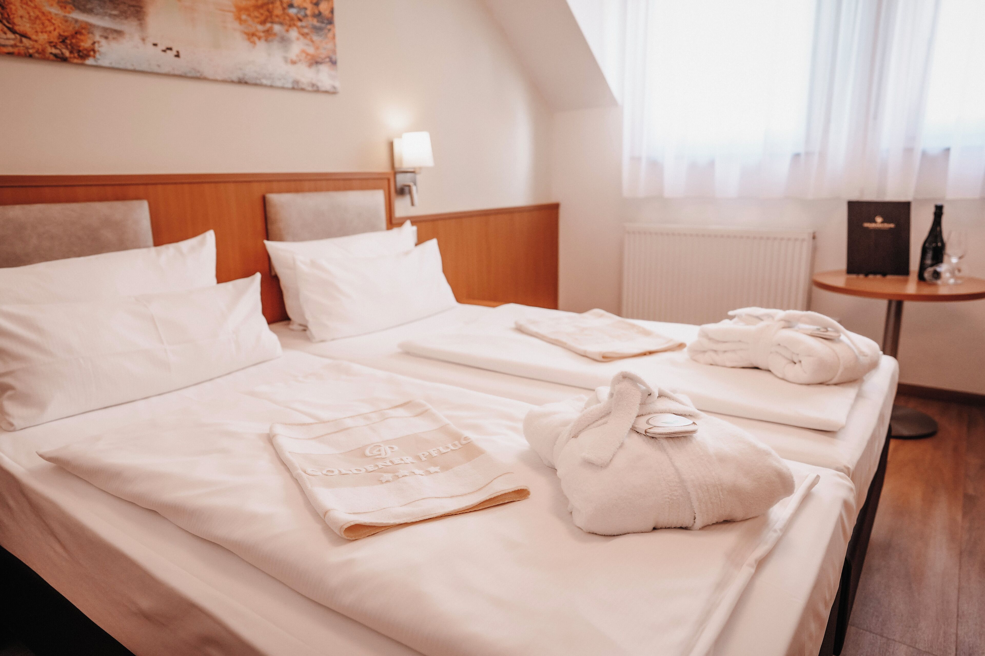 Habitación de hotel con dos camas, ropa de cama blanca, una mesita con una botella y un cuadro en la pared.