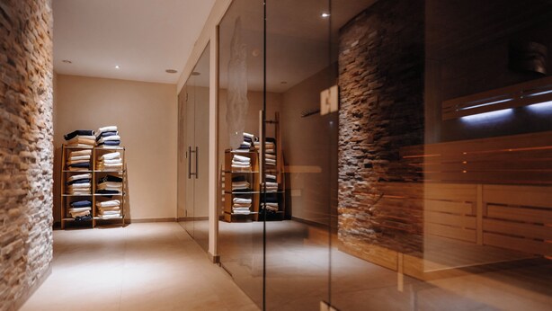 A modern interior with a glass partition, wooden shelving with folded towels, and a stone wall. - Hotel & Restaurant Goldener Pflug (Ludwigsburg)