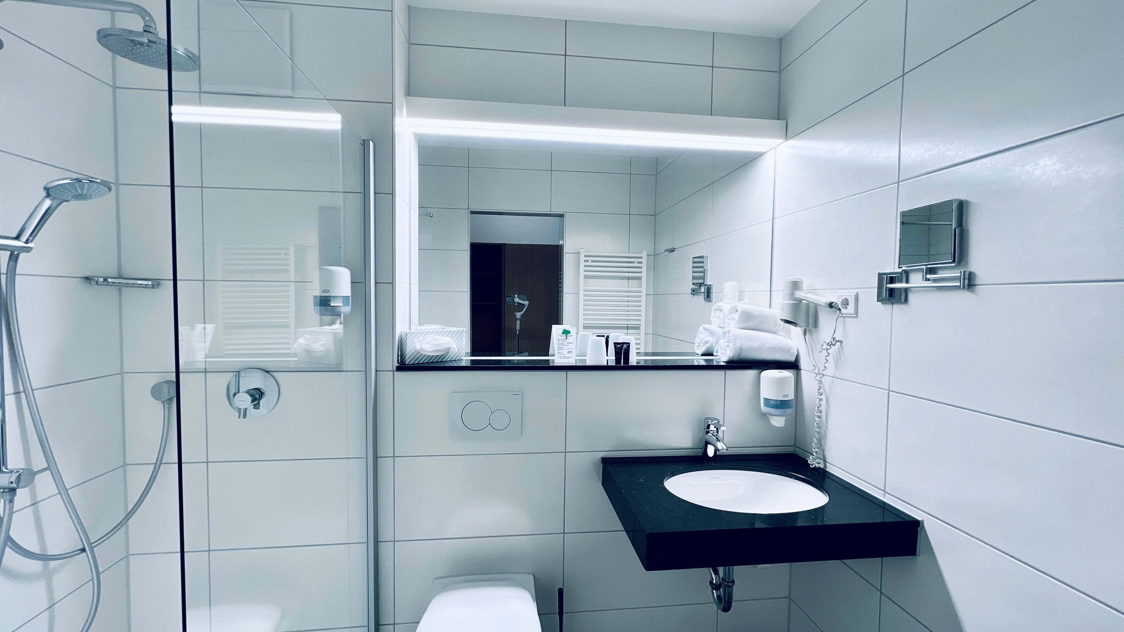 Une salle de bain moderne avec une douche à parois de verre, un lavabo noir et un miroir au-dessus du lavabo.