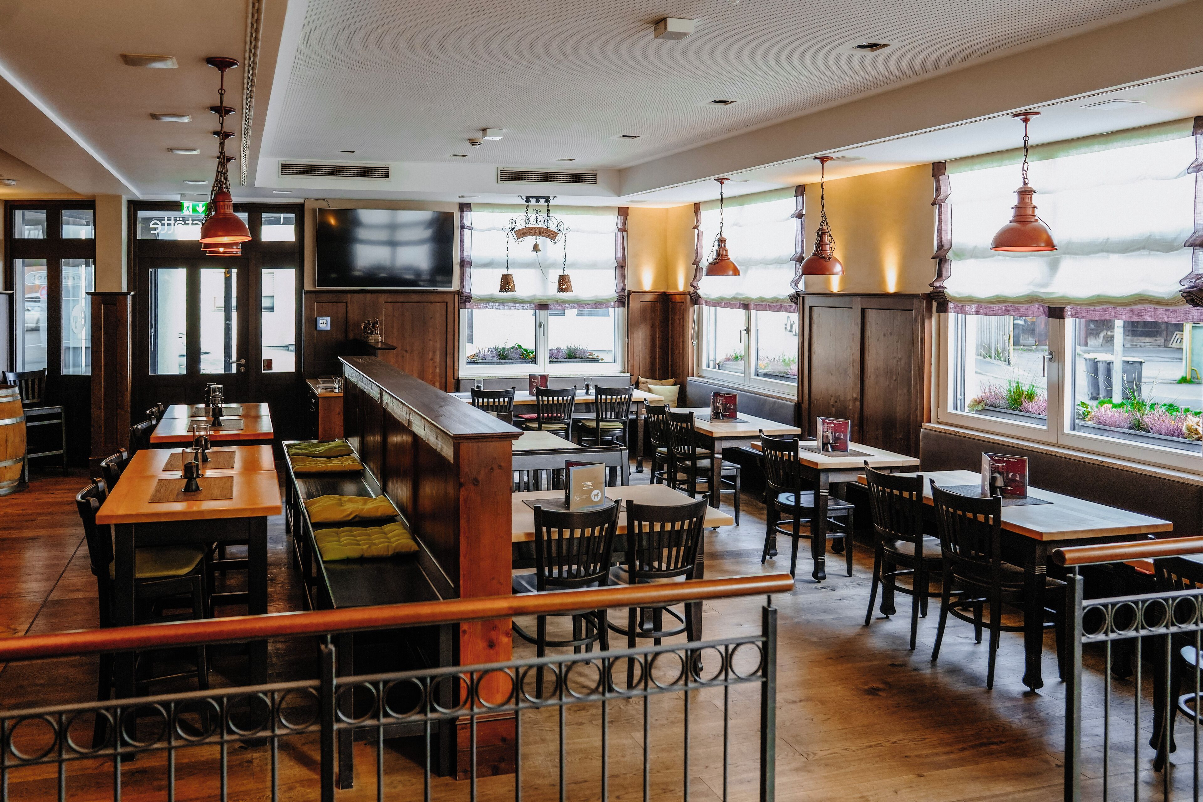 Een restaurant met houten tafels en banken, grote ramen en hangende lampen.