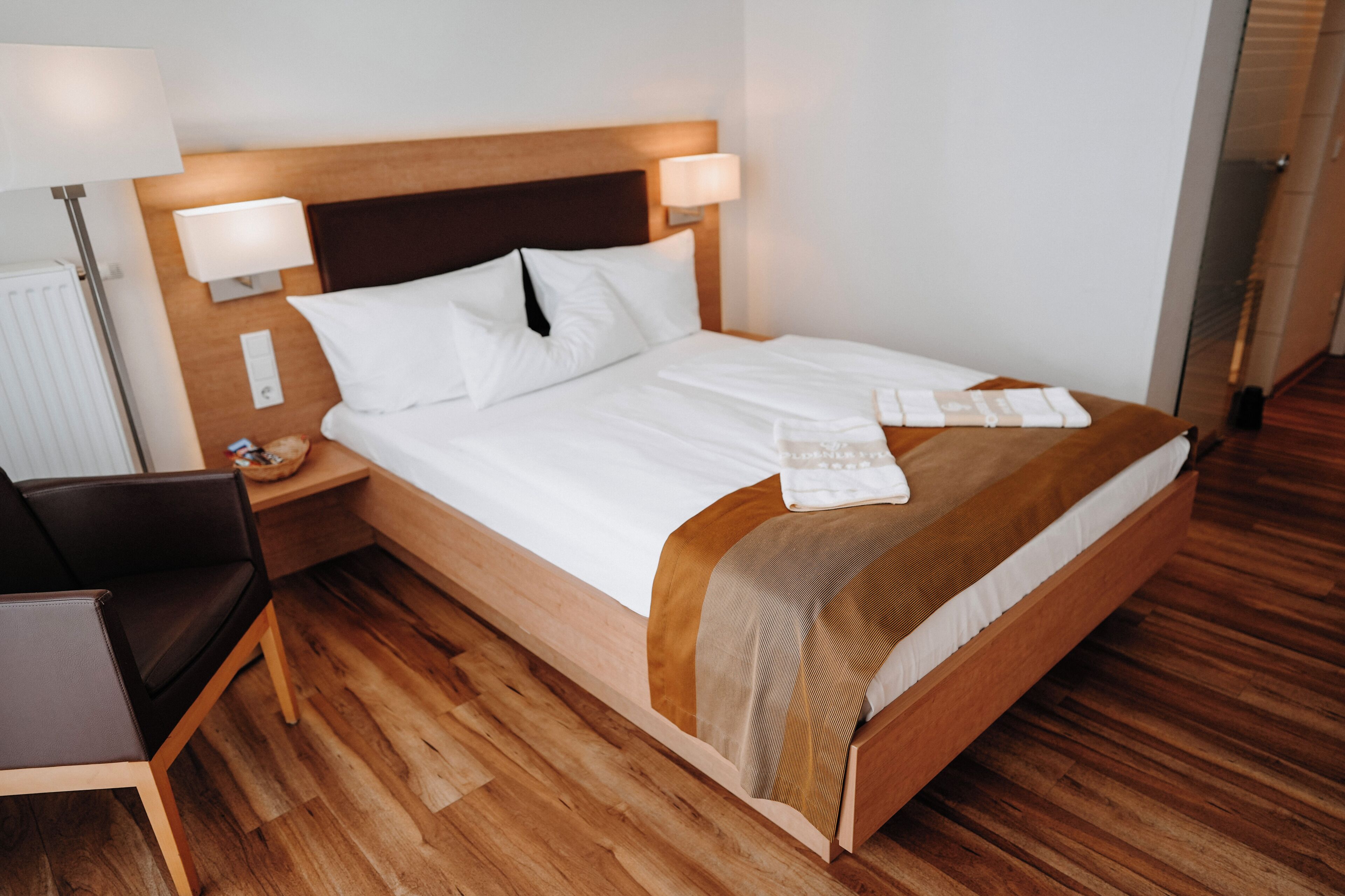 A neatly made bed with white linens, a wooden headboard, and a bedside table with a lamp.