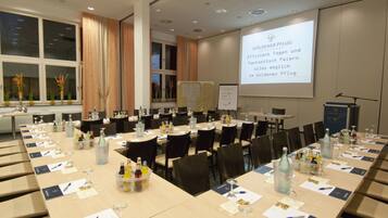 A conference room with long tables, chairs, and a projector screen displaying text.