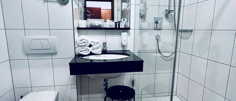 Un baño moderno con inodoro, lavamanos y cabina de ducha con mampara de vidrio.