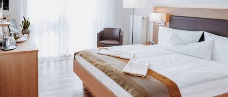 Habitación de hotel con una cama de madera, un escritorio con lámpara, una silla y vistas a la ciudad a través de amplias ventanas.