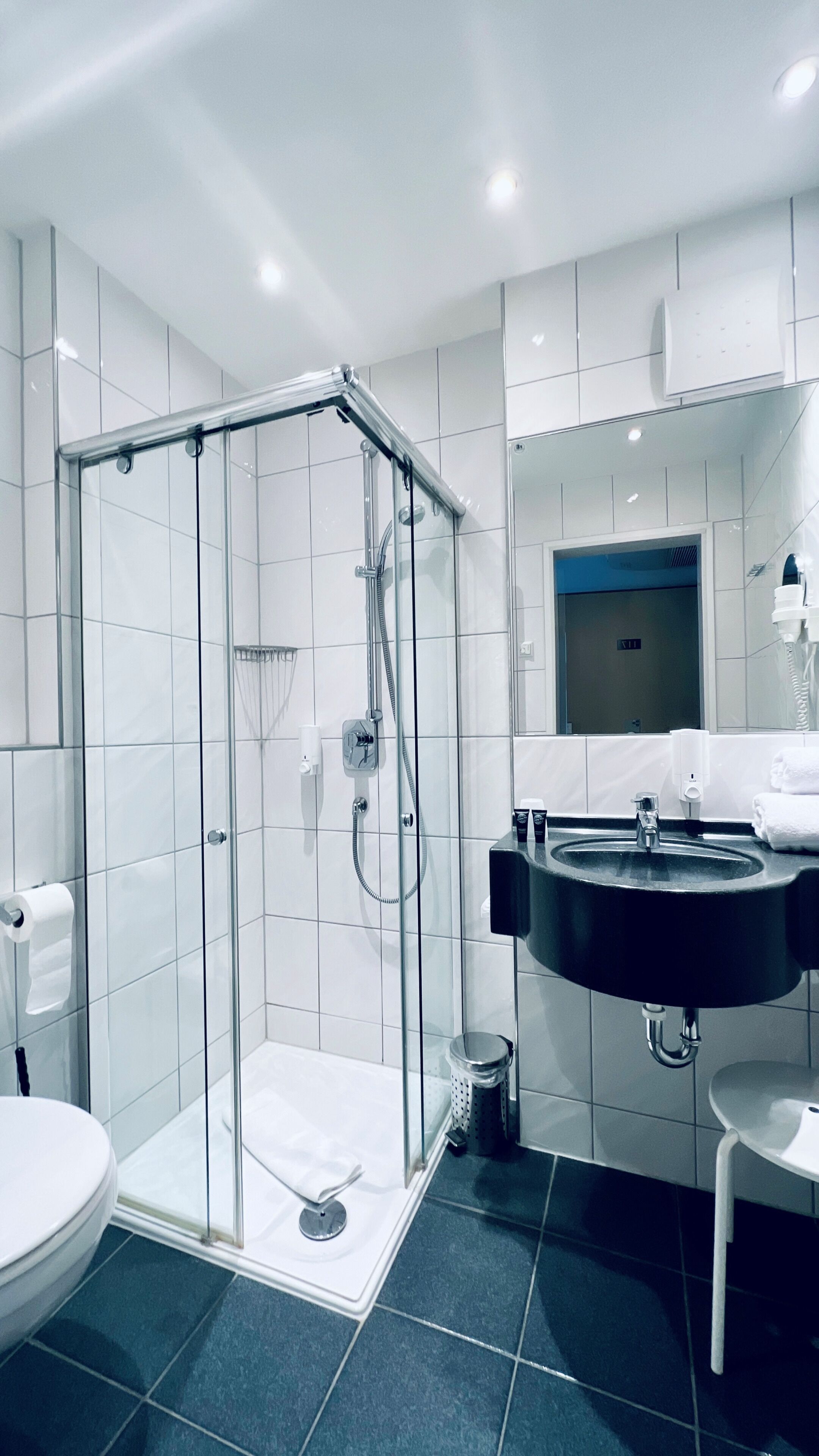 A modern bathroom with a glass-enclosed shower, a black sink, and white tiled walls.