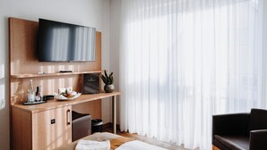 A hotel room with a bed, a desk with a flat-screen TV, a small seating area, and a large window with sheer curtains. - Hotel & Restaurant Goldener Pflug (Ludwigsburg)