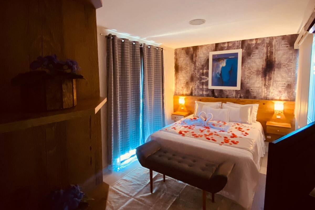 A bedroom with a large bed, two bedside tables with lamps, a wooden headboard, and a painting on the wall.