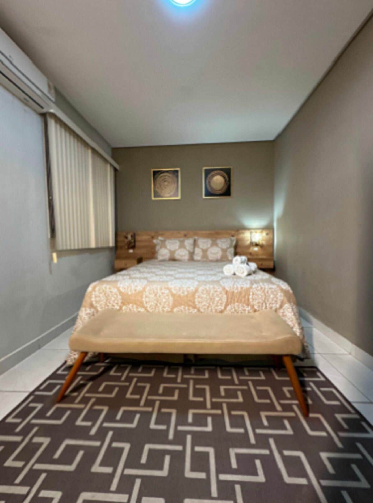 A bedroom with a bed, a window with blinds, a headboard, and two framed pictures on the wall.