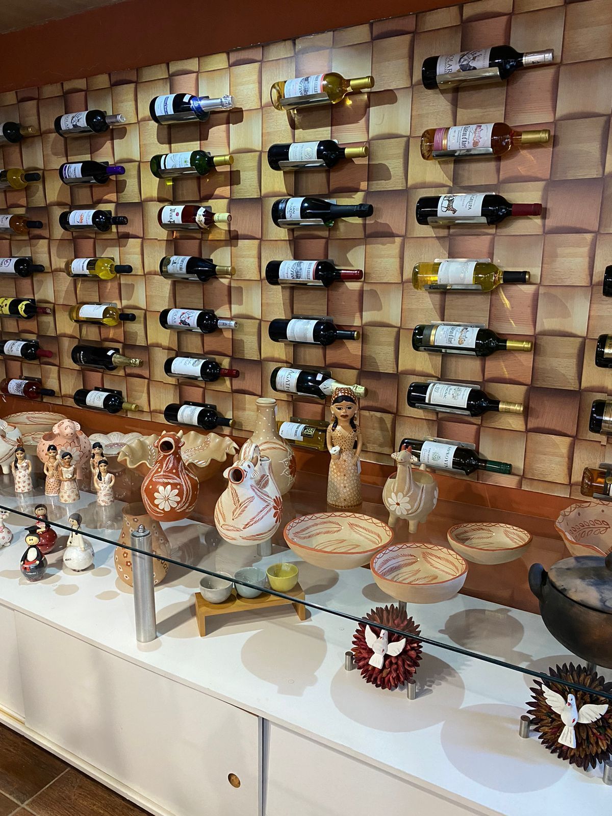 Uma estante para vinhos com diversos garrafas e louças de cerâmica em exposição.