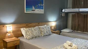 Un dormitorio con una cama litera, una mesita de noche con lámpara, una mesilla auxiliar y un cuadro de una playa.