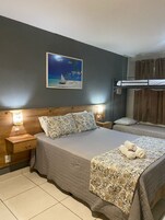 Un dormitorio con una cama litera, una mesita de noche con lámpara, una mesilla auxiliar y un cuadro de una playa.
