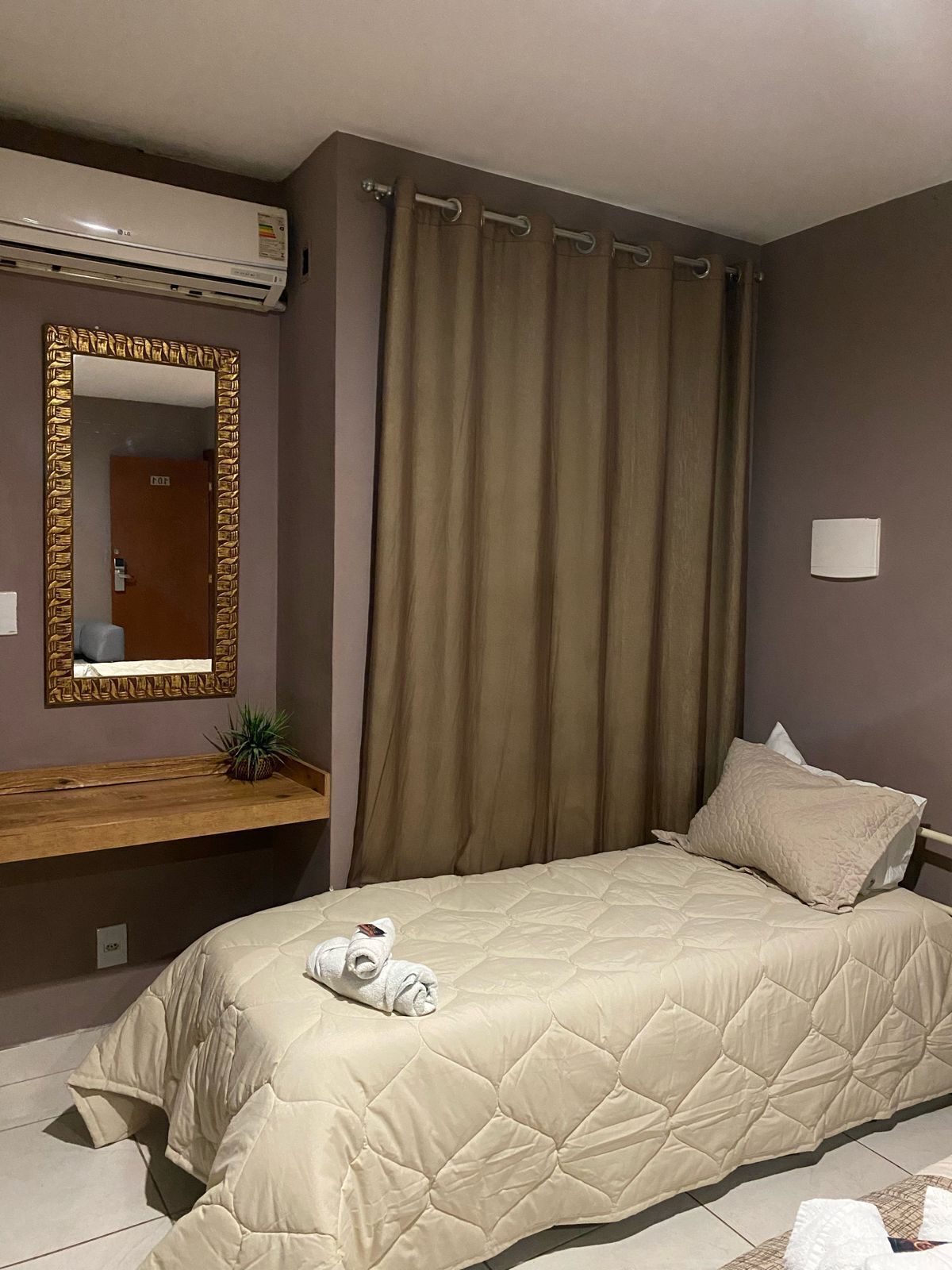 A bedroom with a bed, a mirror, a wooden shelf, and a door.