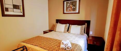 A hotel room with a bed, a bedside table, a chair, and a small table with towels.