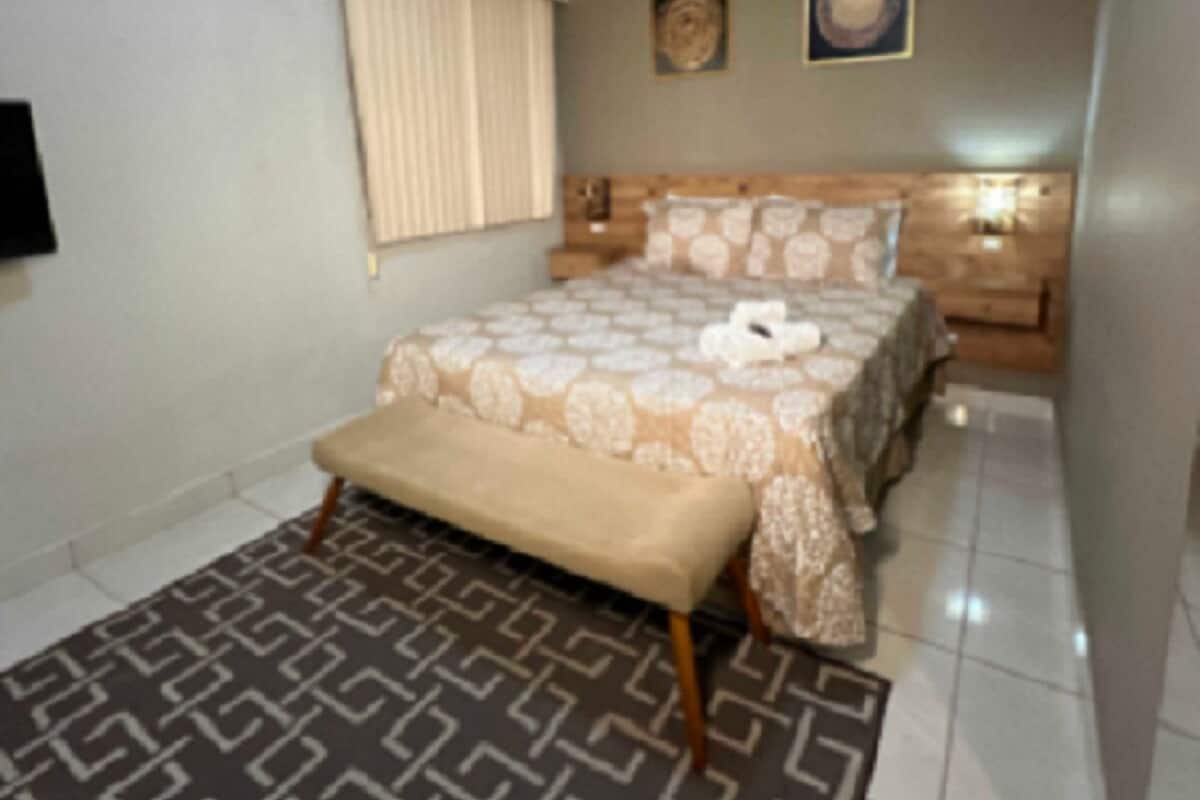 A bedroom with a bed, a bench, a nightstand, a wall-mounted TV, and a ceiling light.