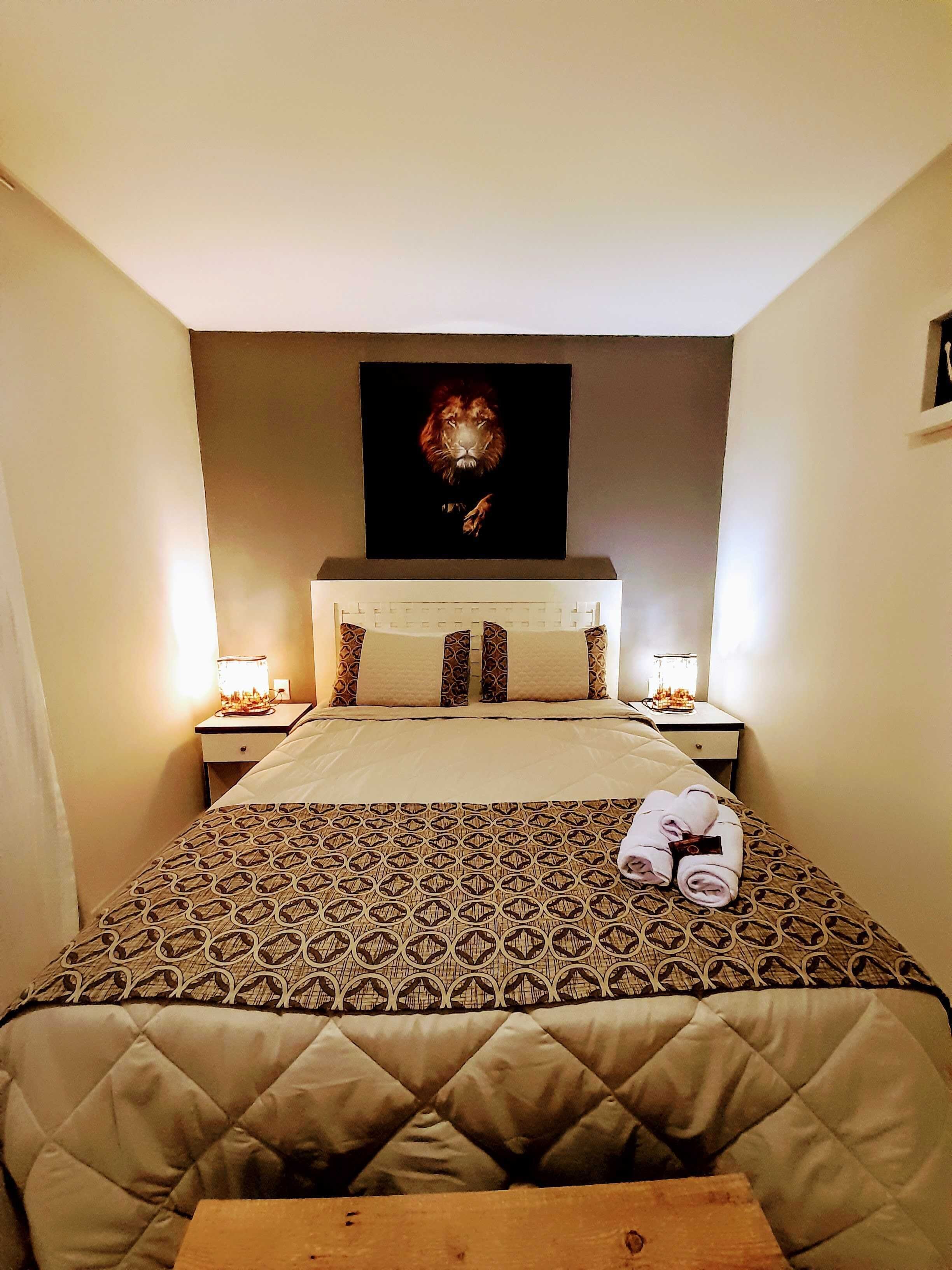 Habitació d'hotel amb un llit gran, un panell del capçal amb una pintura de lleó, dues taules de nit amb làmpades i un edredó acolxat.