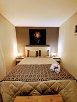 Una habitación de hotel con una cama grande, un cabecero con una pintura de un león, dos mesitas de noche con lámparas y una colcha acolchada.