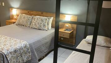 A bedroom with a bunk bed, a single bed, a nightstand with a lamp, and a painting on the wall.