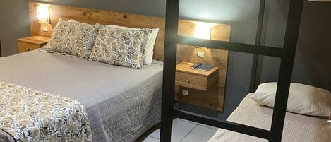 A bedroom with a bunk bed, a single bed, a nightstand with a lamp, and a painting on the wall.
