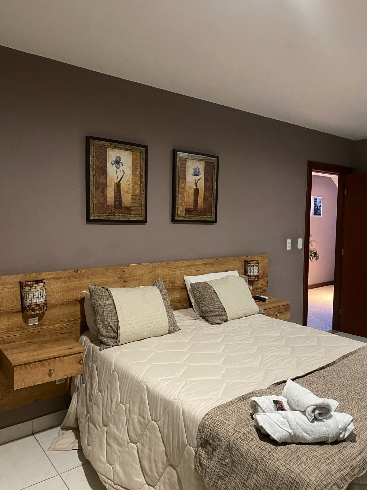 A bedroom with a wooden headboard, a large bed with a quilted cover, two bedside tables, and two framed pictures on the wall.